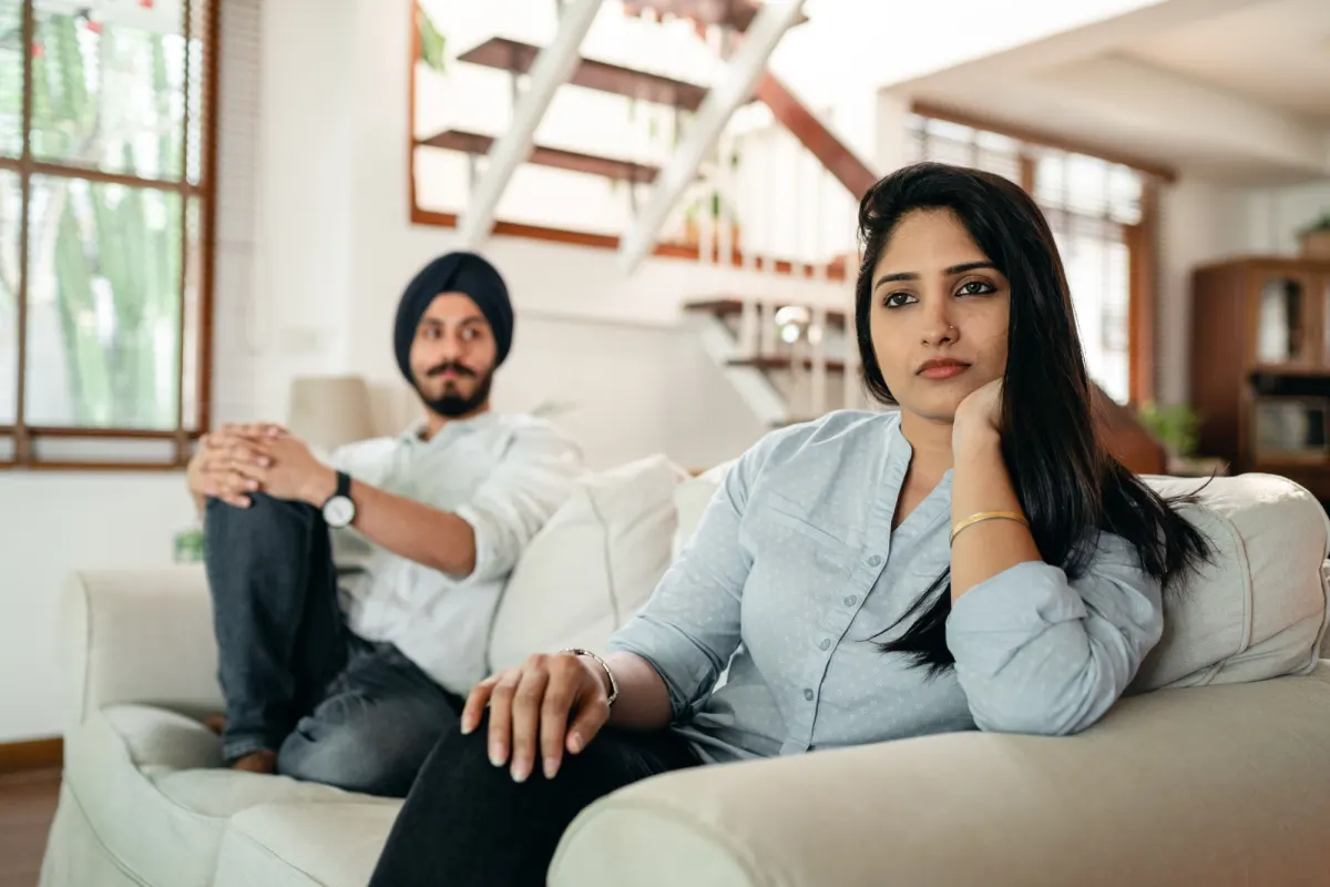 A couple sitting apart on a sofa at home, the woman looking away as the man glances towards her