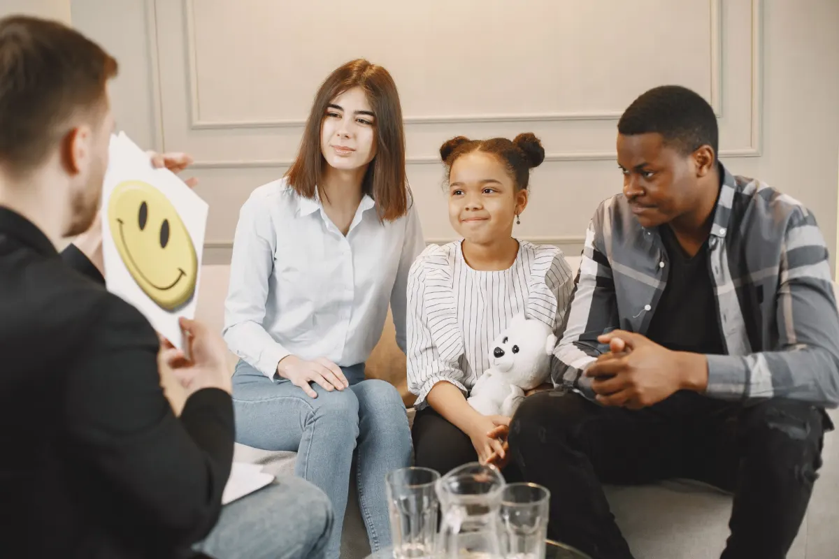 Two parents and their young daughter sitting together on a sofa, talking with a therapist