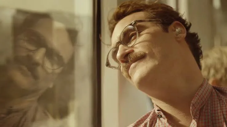 Joaquin Phoenix as Theodore in Her, smiling with his head against a train window, earpiece in
