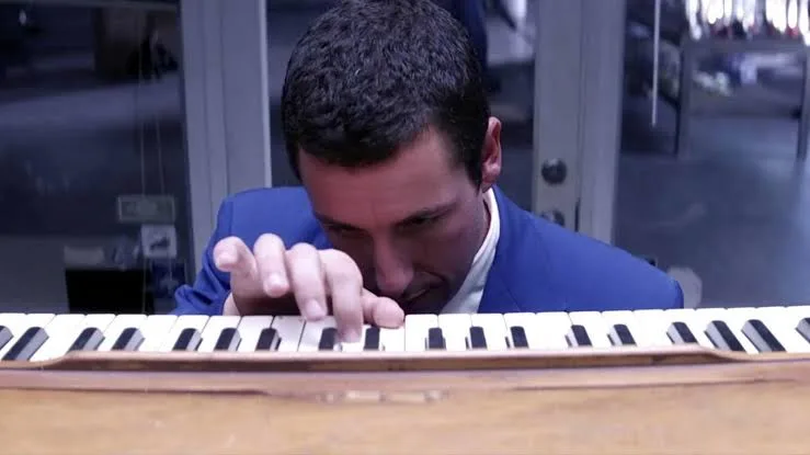 Adam Sandler as Barry Egan in Punch-Drunk Love, hunched intently over a harmonium in a dim warehouse