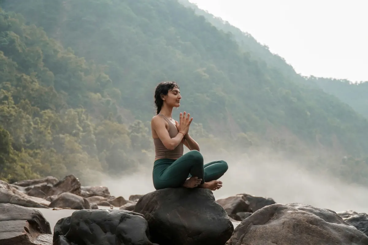 A woman meditating cross-legged on a rock in a misty river valley
