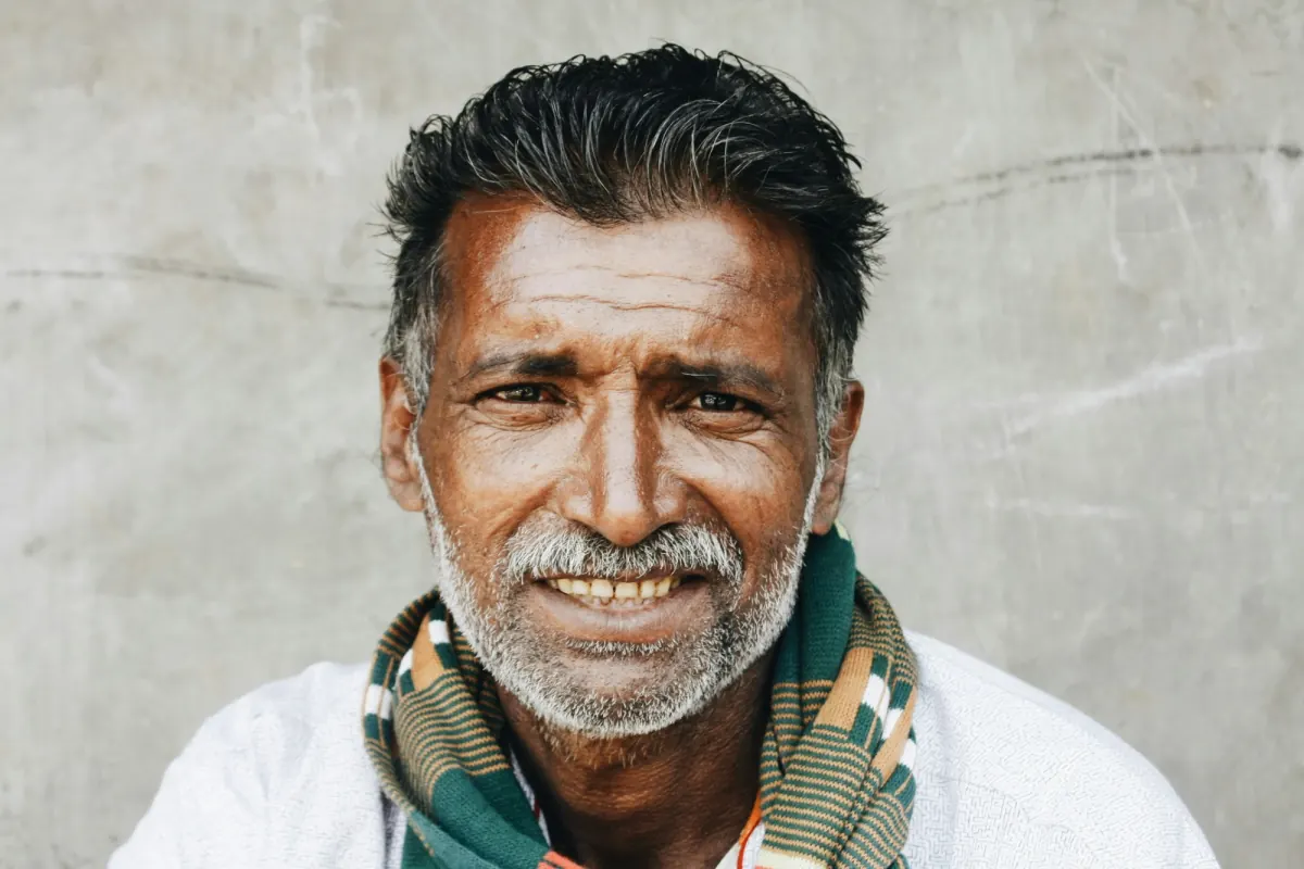 Portrait of a smiling older Indian man with a grey beard and a striped scarf