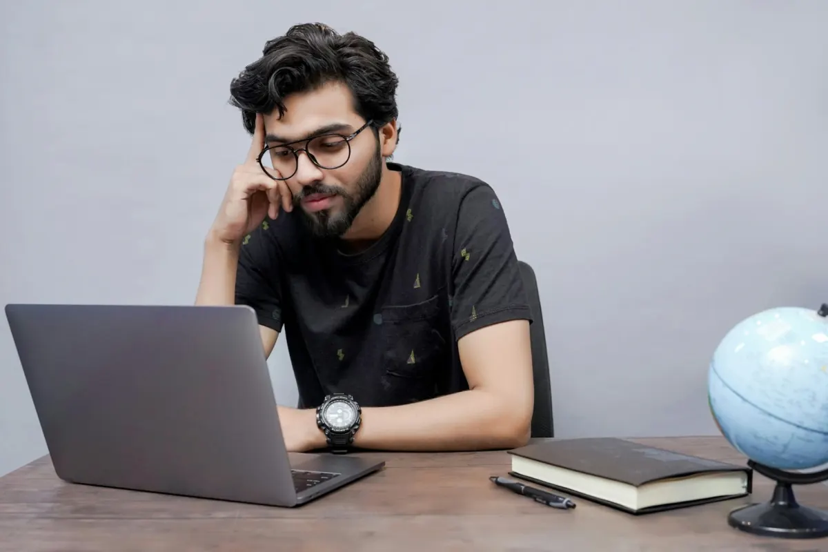 A young Indian man with glasses at a laptop, head resting on his hand