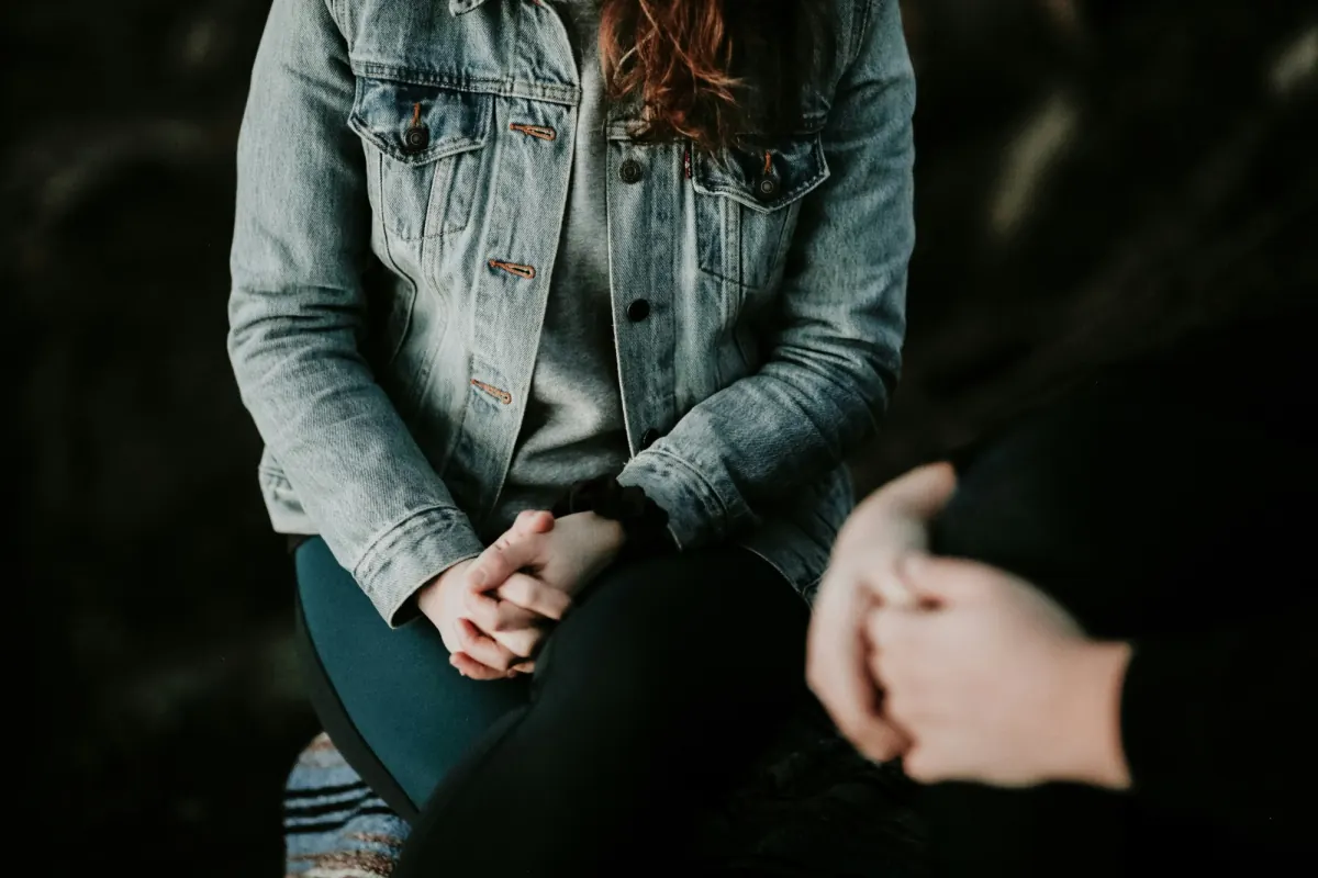 Two people seated facing each other in conversation, one with hands clasped