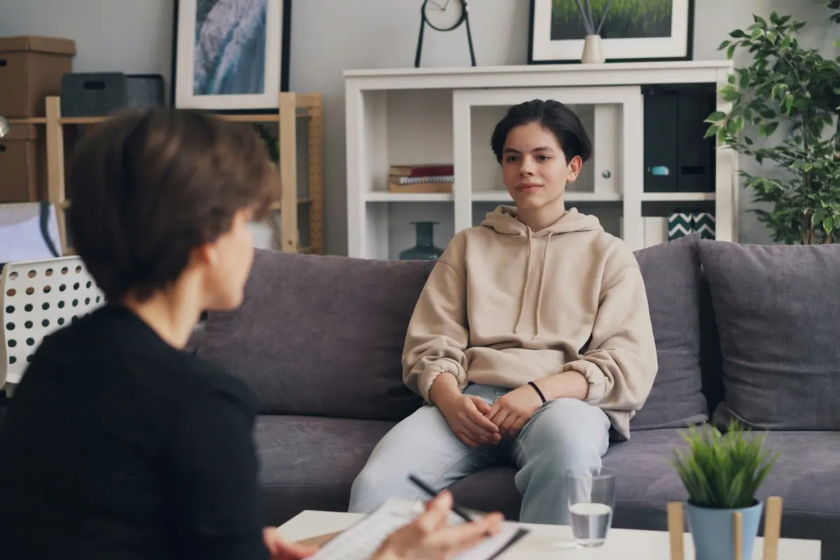 A young person on a sofa talking with a clinician who is taking notes