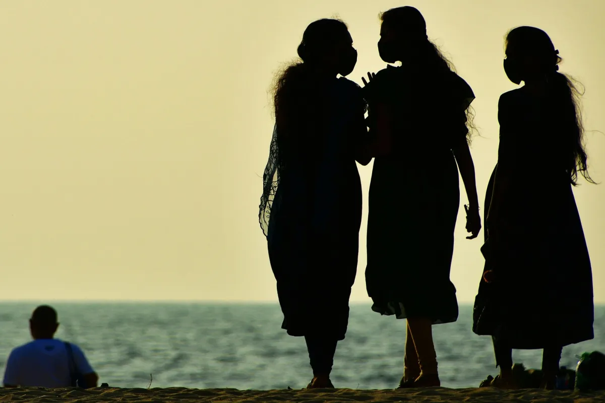 Three women in silhouette talking together on a beach at sunset, the sea behind them